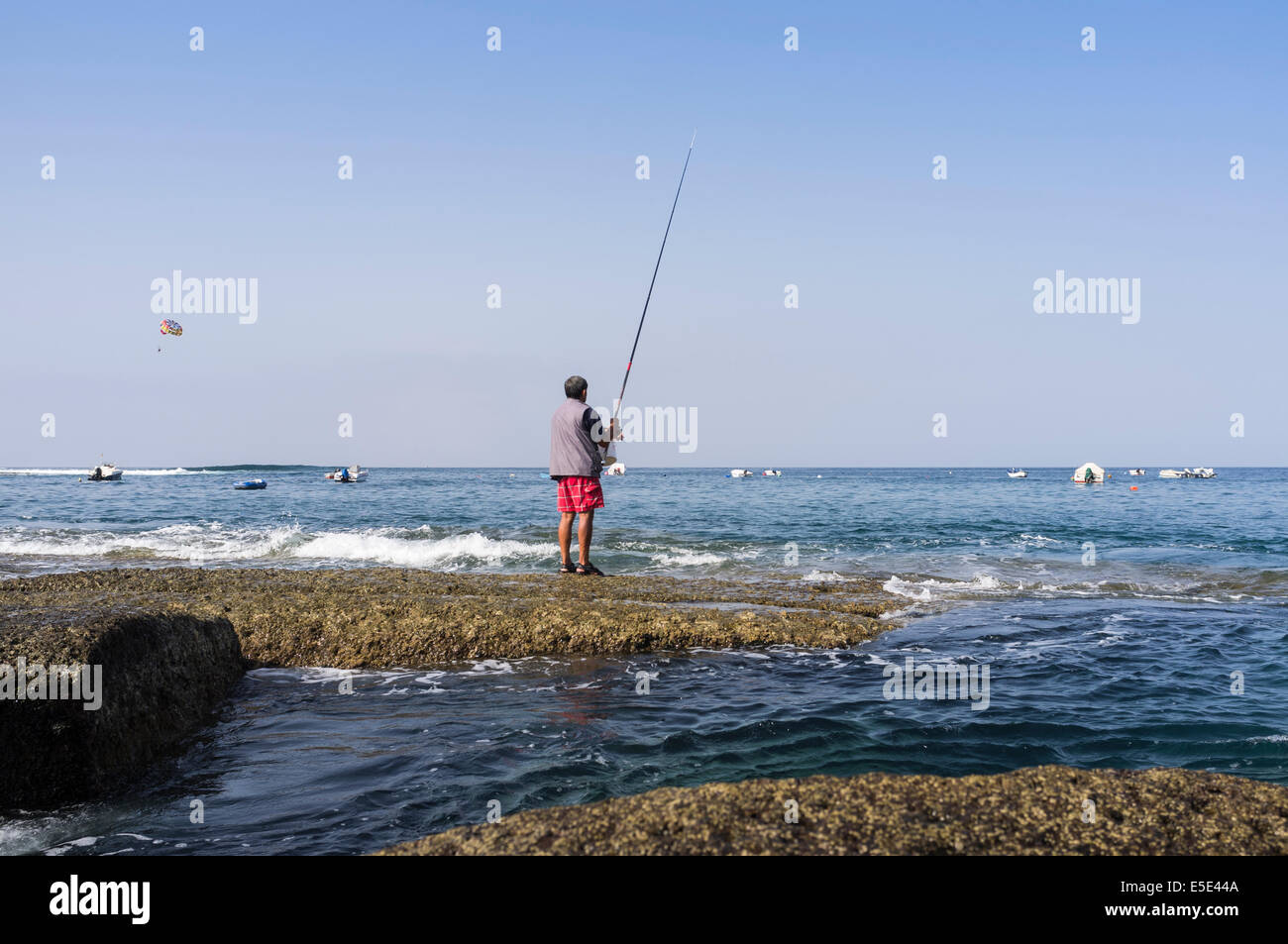 Fischer Angeln von den Felsen an der Küste in La Caleta, Costa Adeje, Teneriffa, Kanarische Inseln, Spanien. Rennrodel-Boot mit Stockfoto
