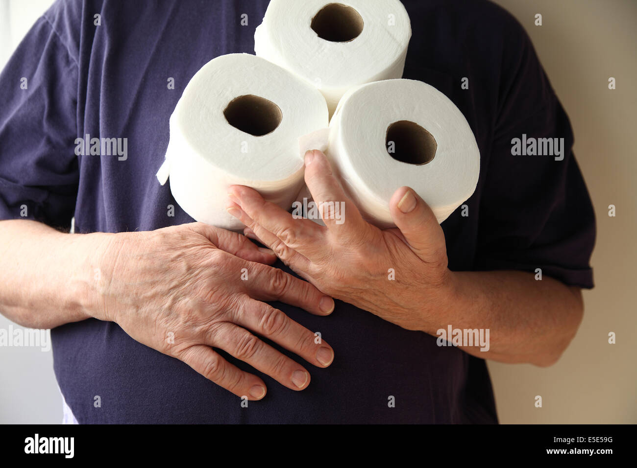 Mann hat Magenbeschwerden und hält drei Rollen Toilettenpapier Stockfoto