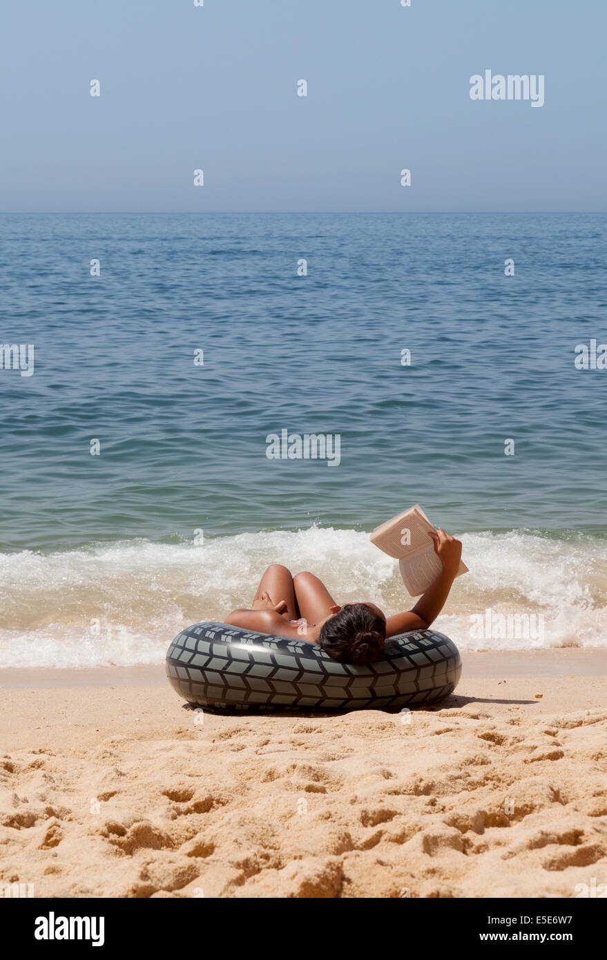 Frau, die sich im Urlaub entspannt, ein Buch am Strand am Ufer der Algarve, Portugal, Europa liest Stockfoto