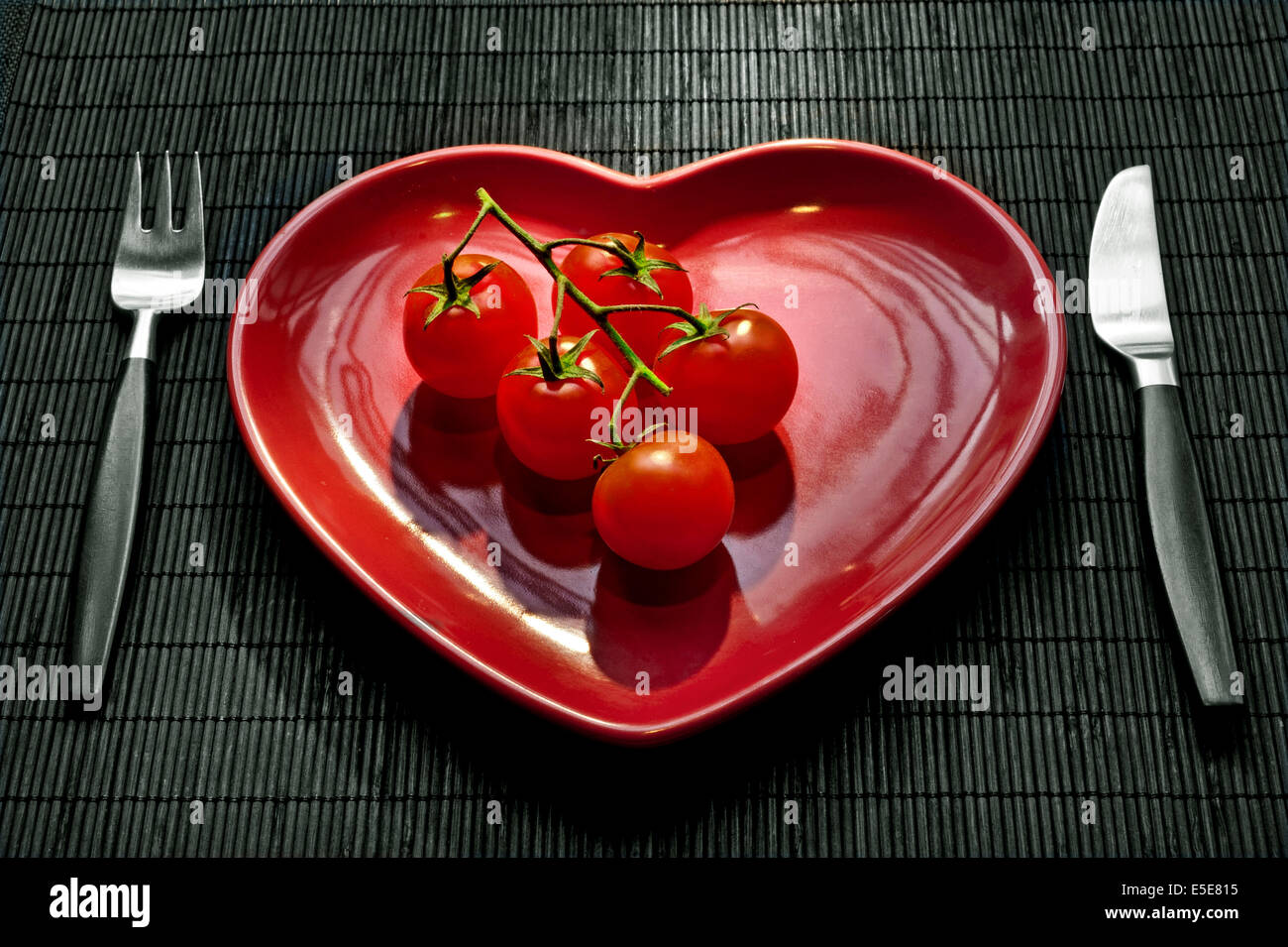 Gesunde frische Ernährung Regime Konzept mit Reife strauchtomaten auf roten herzförmigen Platte und Tischdekoration Stockfoto