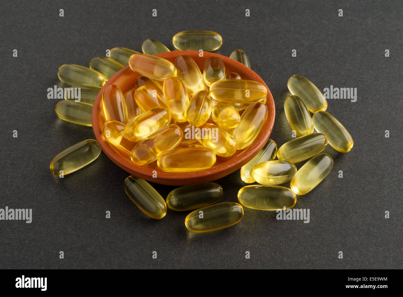 Eine kleine Schüssel mit Kabeljau Leber Öl-Kapseln mit mehreren verstreut auf einem dunklen Hintergrund. Stockfoto