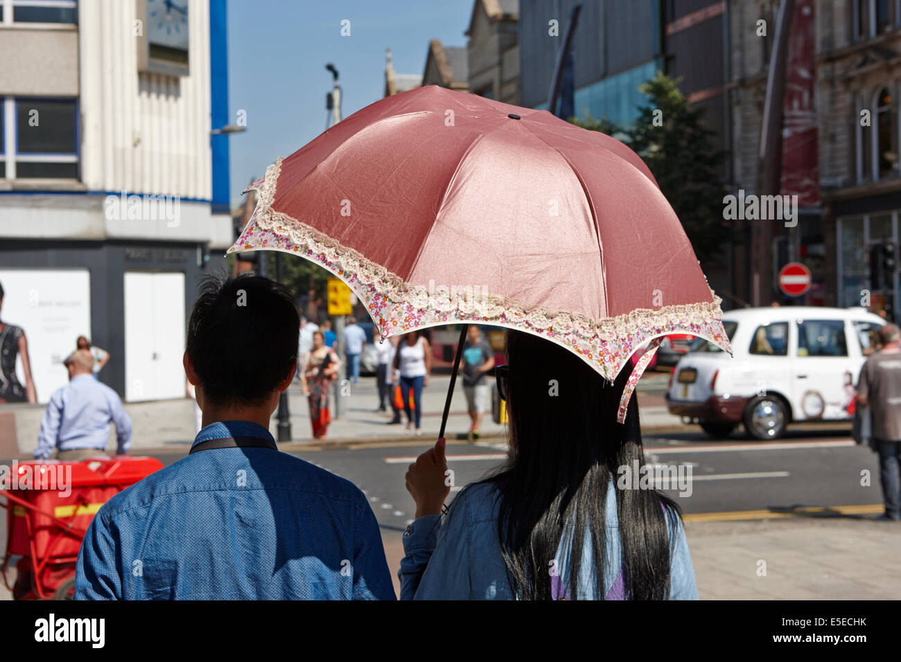 männliche und weibliche asiatische Touristen-paar mit einem Sonnenschirm an einem heißen sonnigen Sommertag im Stadtzentrum von Belfast Stockfoto
