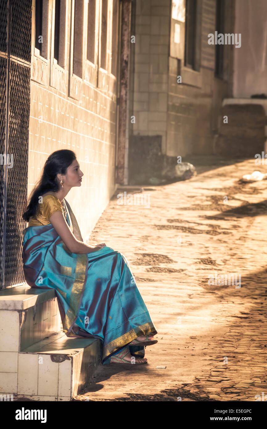 Eine junge Frau in einem Saree sitzt auf einem Schritt auf einer gepflasterten Straße in alten Mumbai, Indien Stockfoto