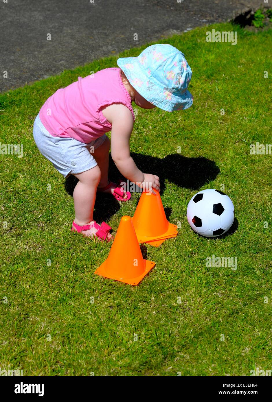 Kleinkind Mädchen trägt einen blauen Sonnenhut Interaktion mit orangen Kegeln Stockfoto