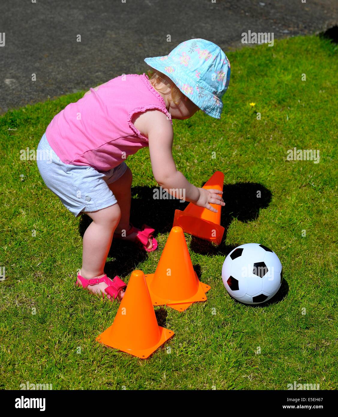Kleinkind Mädchen trägt einen blauen Sonnenhut Interaktion mit orangen Kegeln Stockfoto