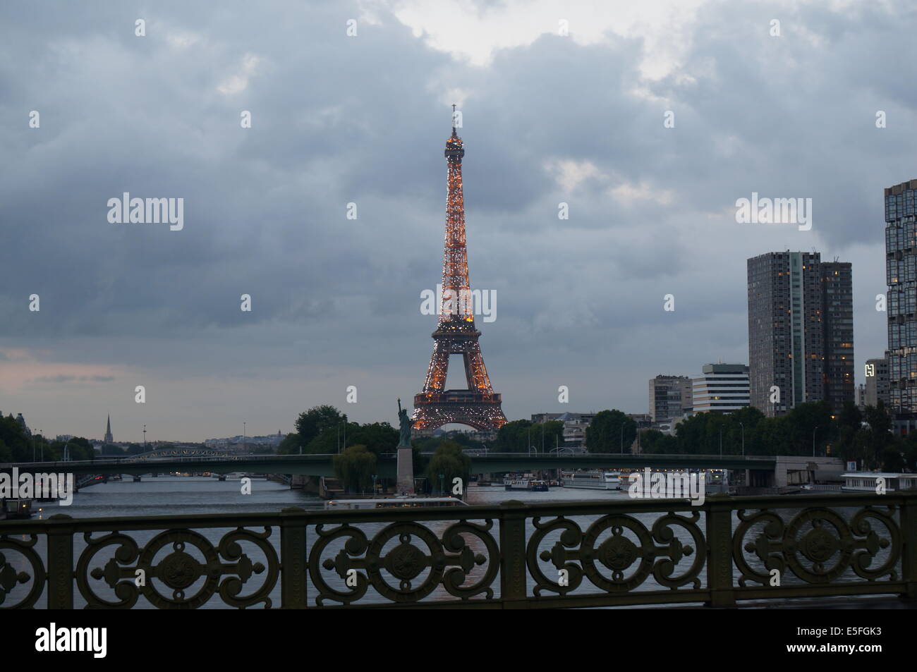 Eiffelturm in der frühen Nacht, beleuchtet mit weißen und orangefarbenen Licht mit der Nachbildung der Freiheitsstatue im Vordergrund Stockfoto