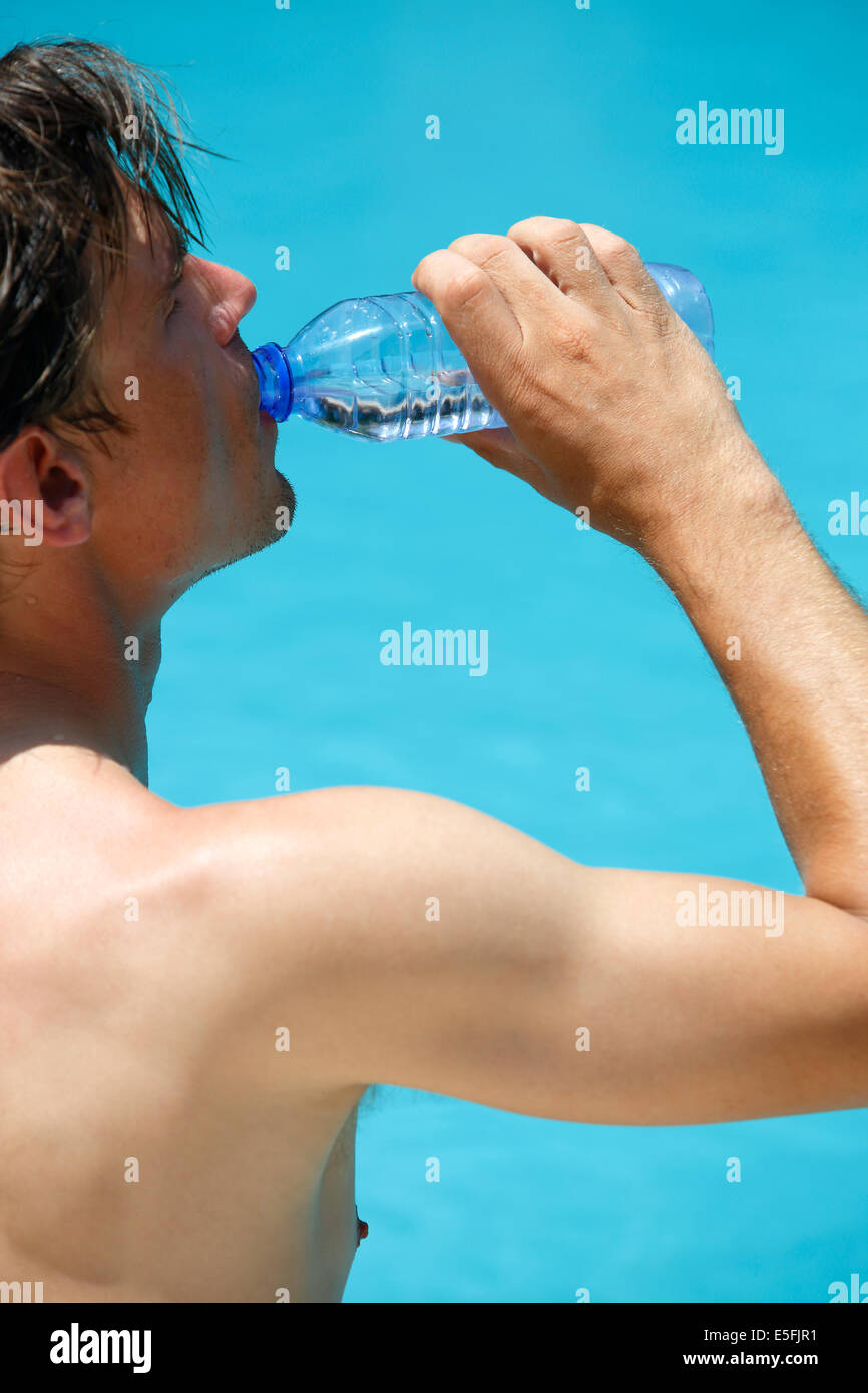 Attraktiver Mann mit blauen Badeanzug trinkt Wasser in einem Schwimmbad Stockfoto