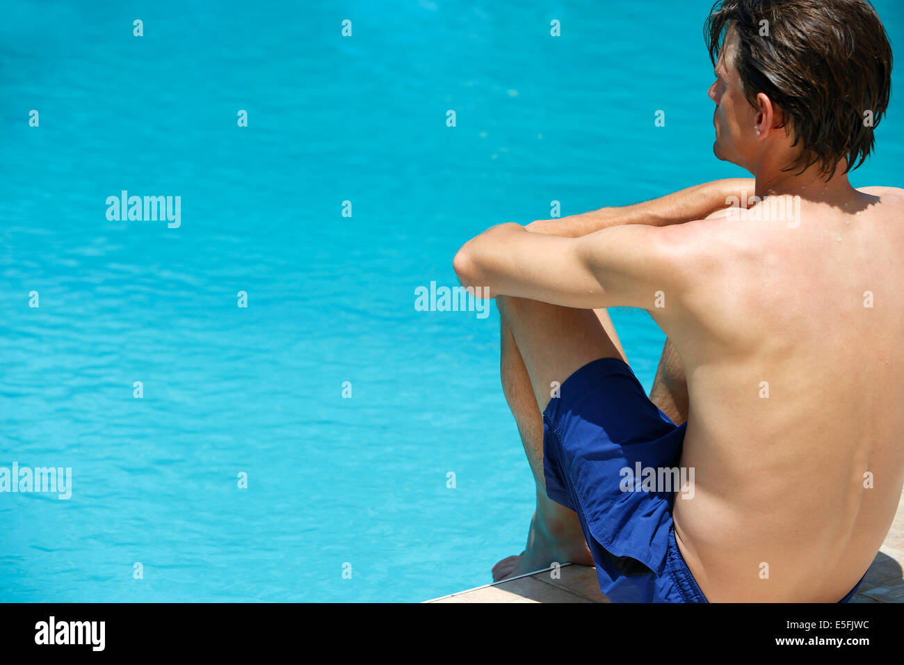 Attraktiver Mann mit blauen Badeanzug genießt Sonne am Pool im Urlaub Stockfoto