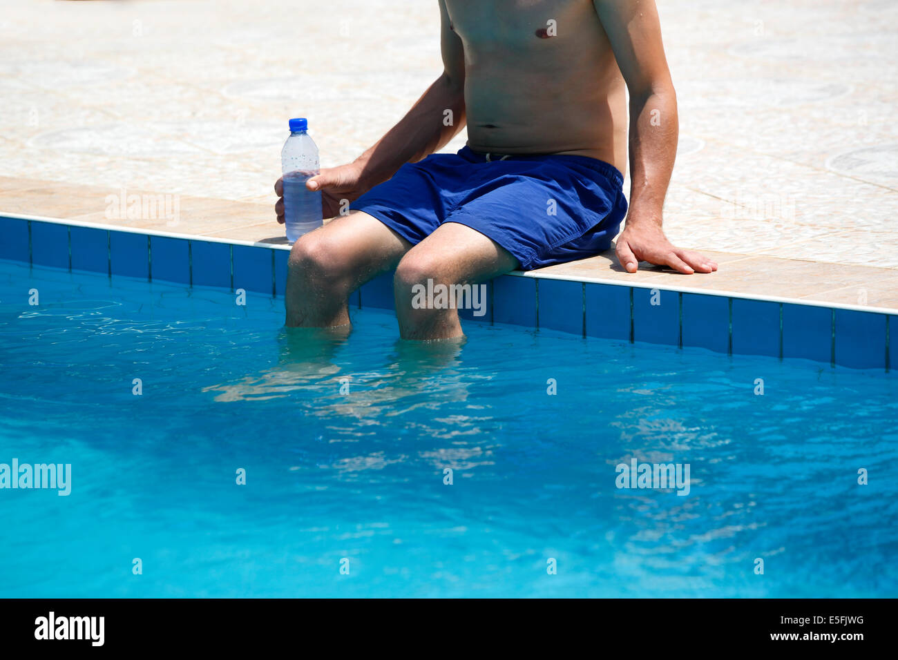 Attraktiver Mann mit blauen Badeanzug und eine Flasche Wasser genießt Sonne in einem Schwimmbad Stockfoto