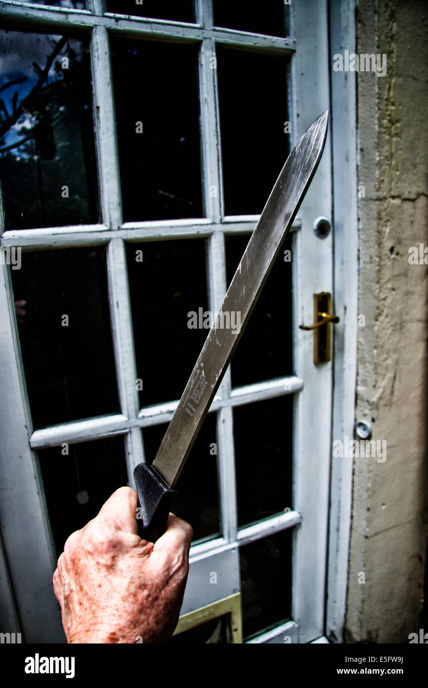 Männliche Hand, die ein großes Küchenmesser Annäherung an die Tür zu einem Haus Stockfoto