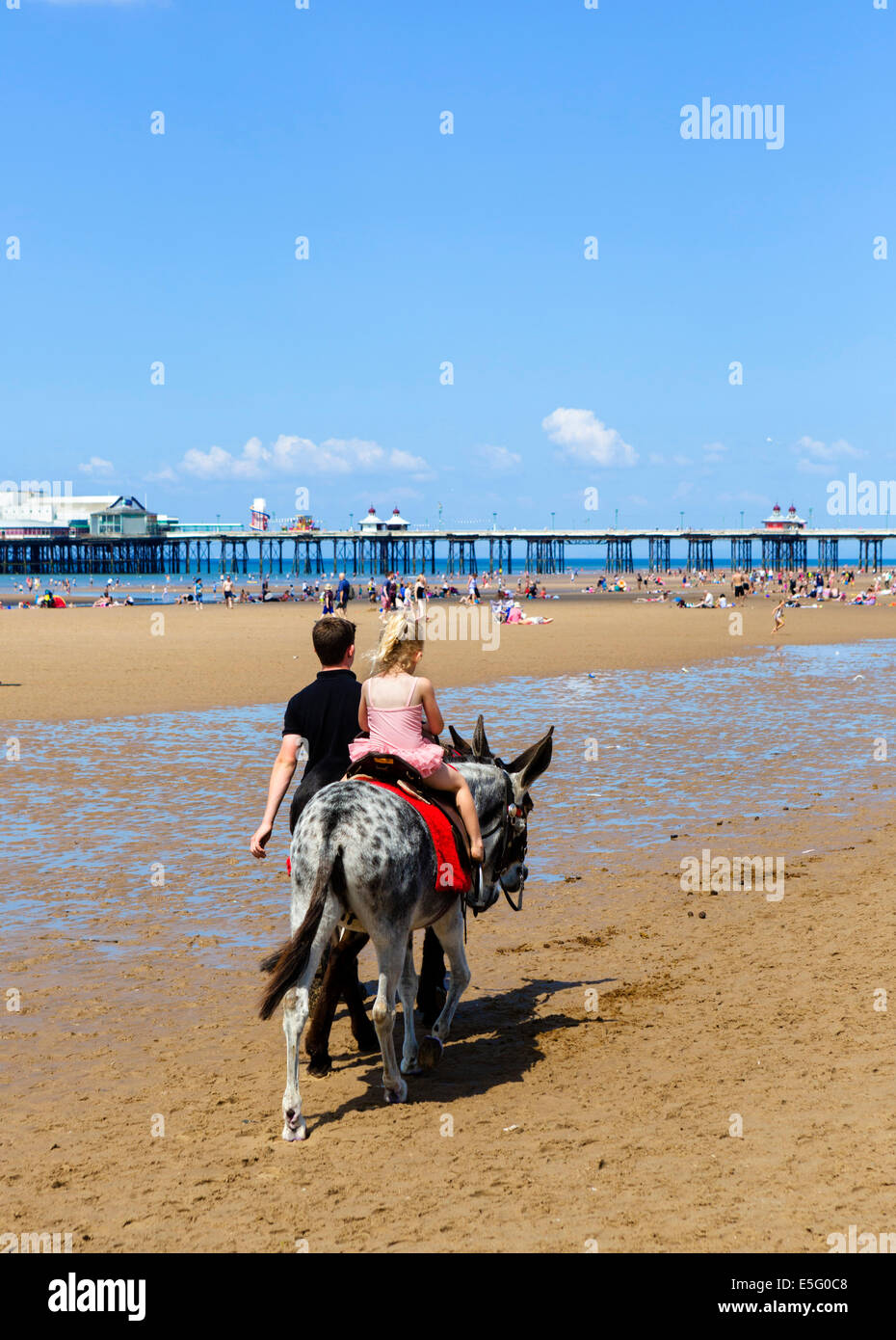 Junges Mädchen auf einem Esel reiten mit North Pier hinter The Golden Mile, Blackpool, Lancashire, UK Stockfoto