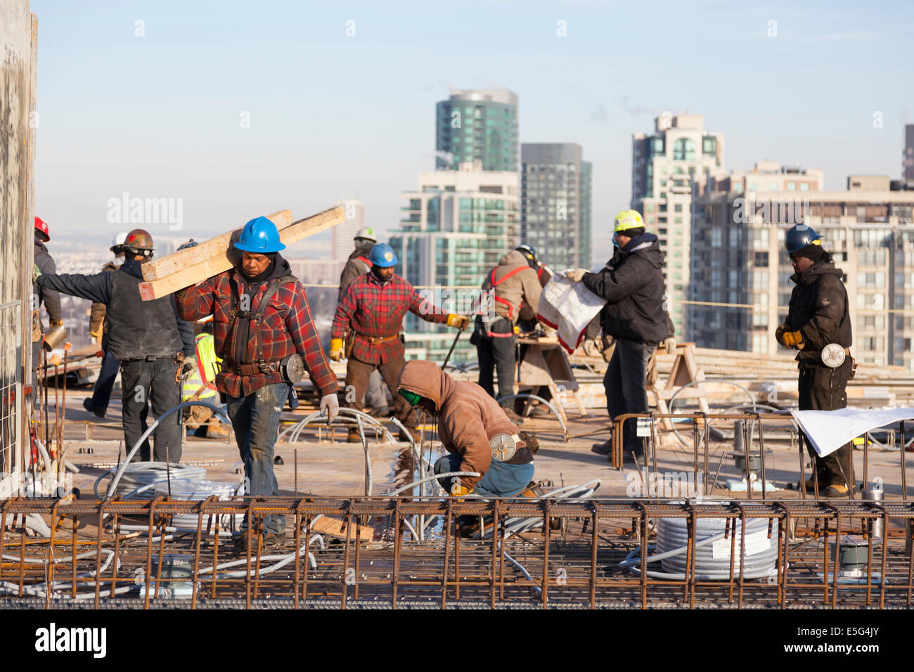 Ein Bauarbeiter tragen eine Last von Bauholz mit anderen Arbeitnehmern im Hintergrund auf einer Baustelle auf dem Dach in Toronto. Stockfoto