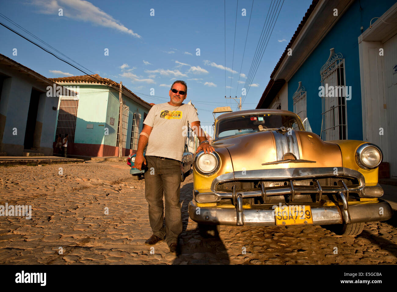 stolzer kubanischen Mann mit seinem US-Oldtimer über eine gepflasterte Straße in der alten Stadt von Trinidad, Kuba, Karibik Stockfoto