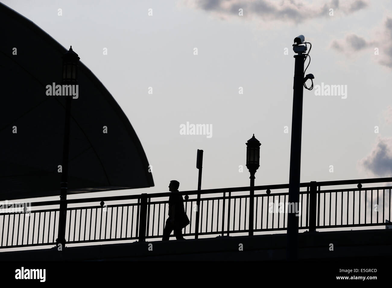 Ein Fußgänger in der Silhouette Spaziergänge unter einer Mast montierte Überwachungskamera. Boston, Massachusetts, Vereinigte Staaten Stockfoto