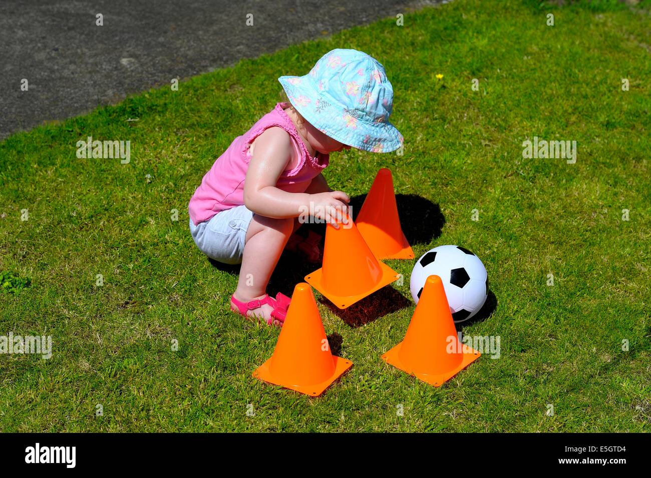 Kleinkind Mädchen trägt einen blauen Sonnenhut Interaktion mit orangen Kegeln Stockfoto