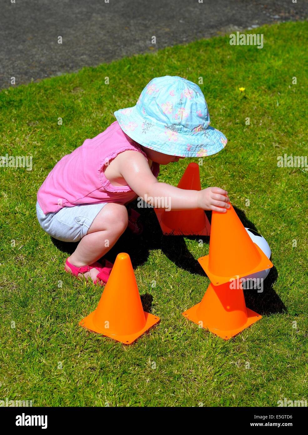 Kleinkind Mädchen trägt einen blauen Sonnenhut Interaktion mit orangen Kegeln Stockfoto