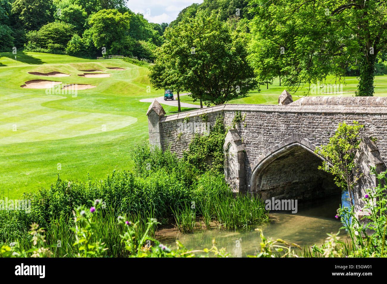 Stein-Brücke über einen Bach durch einen Golfplatz mit Bunkern jenseits. Stockfoto