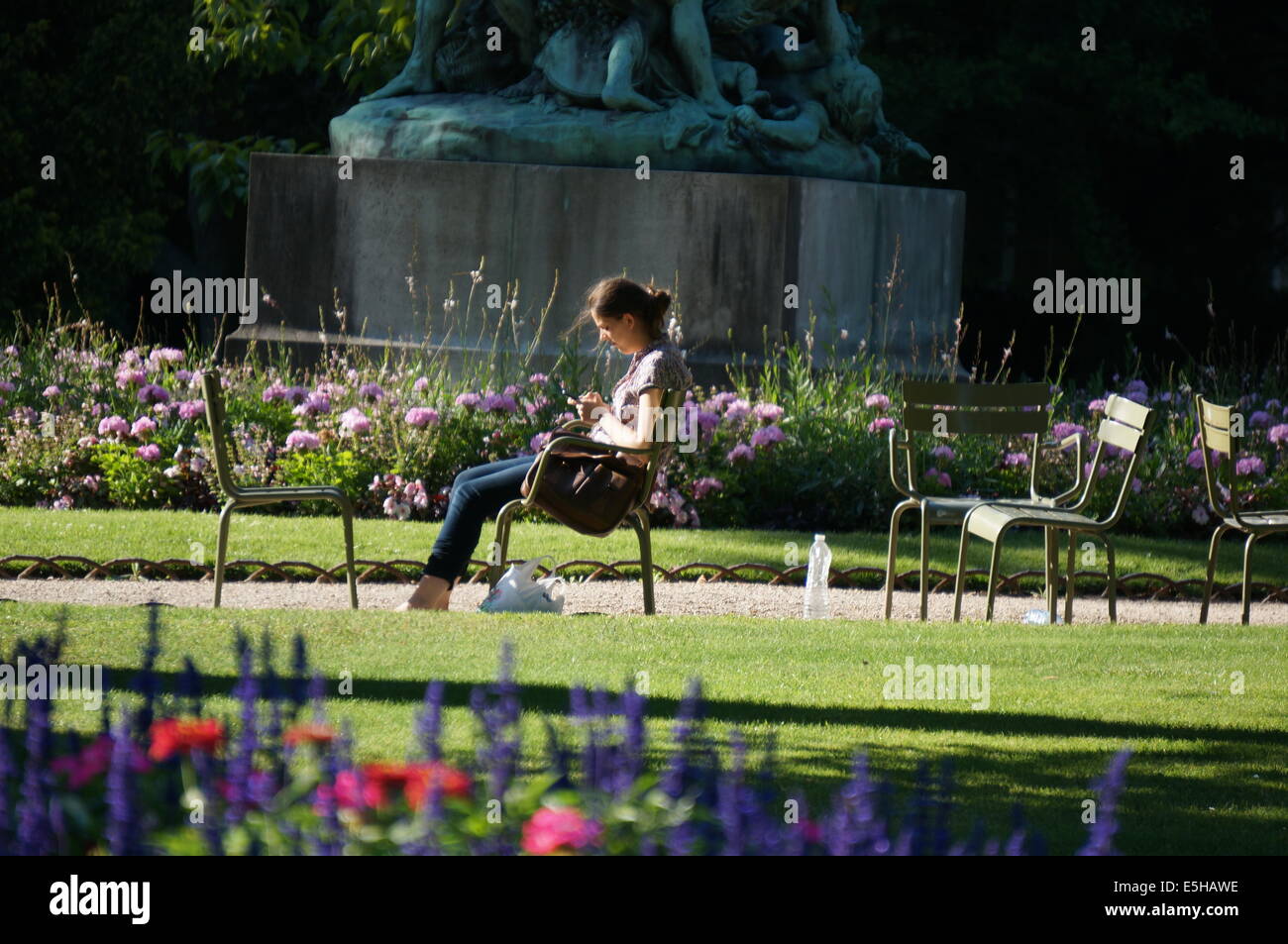 Ein Mädchen in einem Stuhl auf einem Kiesweg zwischen Wiesen, mit Blumenbeeten an einem sonnigen Nachmittag im Jardin du Luxembourg Garden entspannen Stockfoto