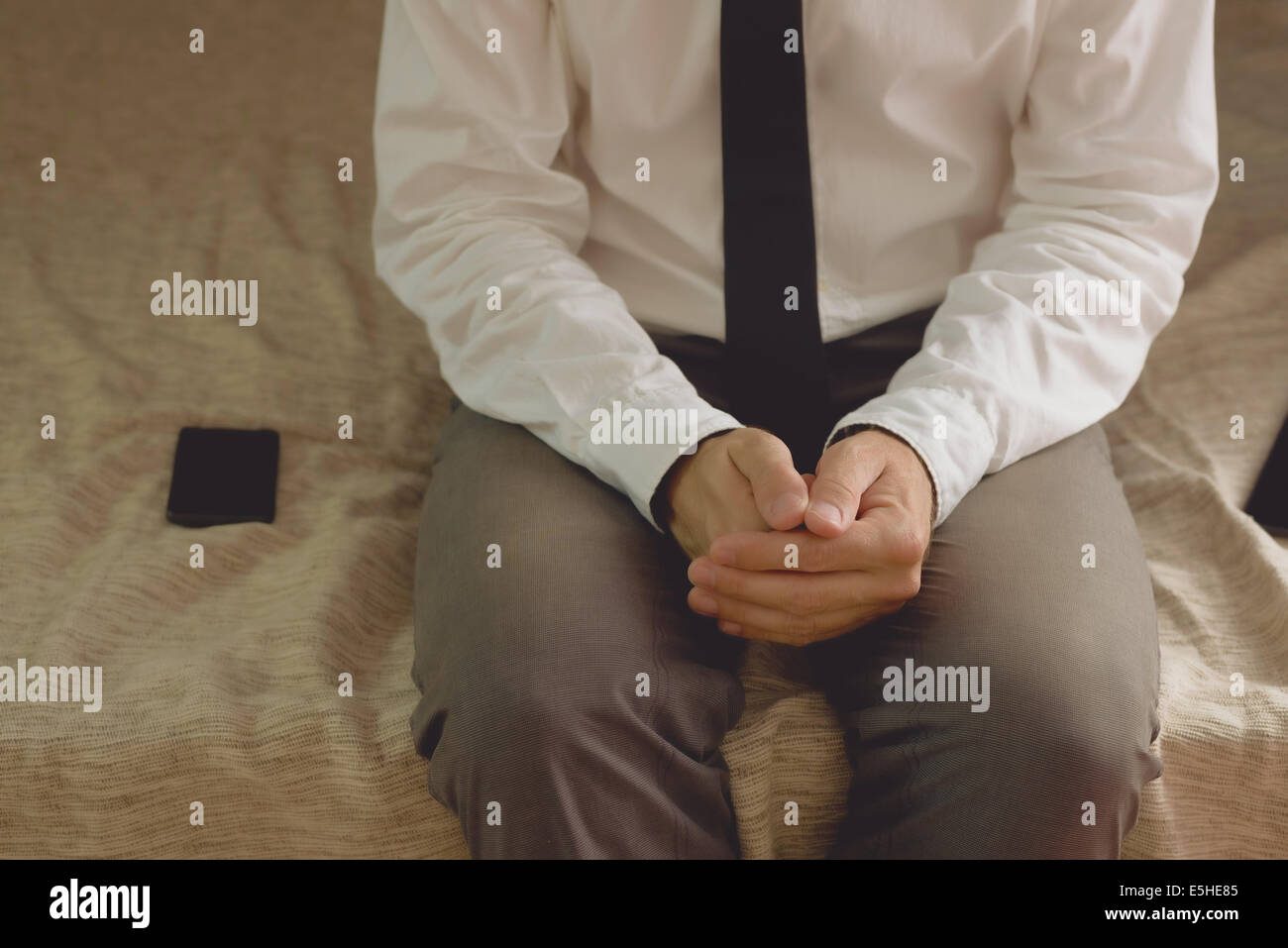 Einsamer Geschäftsmann im Hotelzimmer auf dem Bett sitzend mit Hände gekreuzt Stockfoto