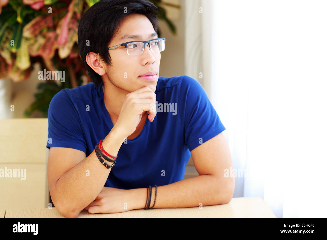 Nachdenklich asiatischen Mann mit Brille, die am Tisch sitzen Stockfoto