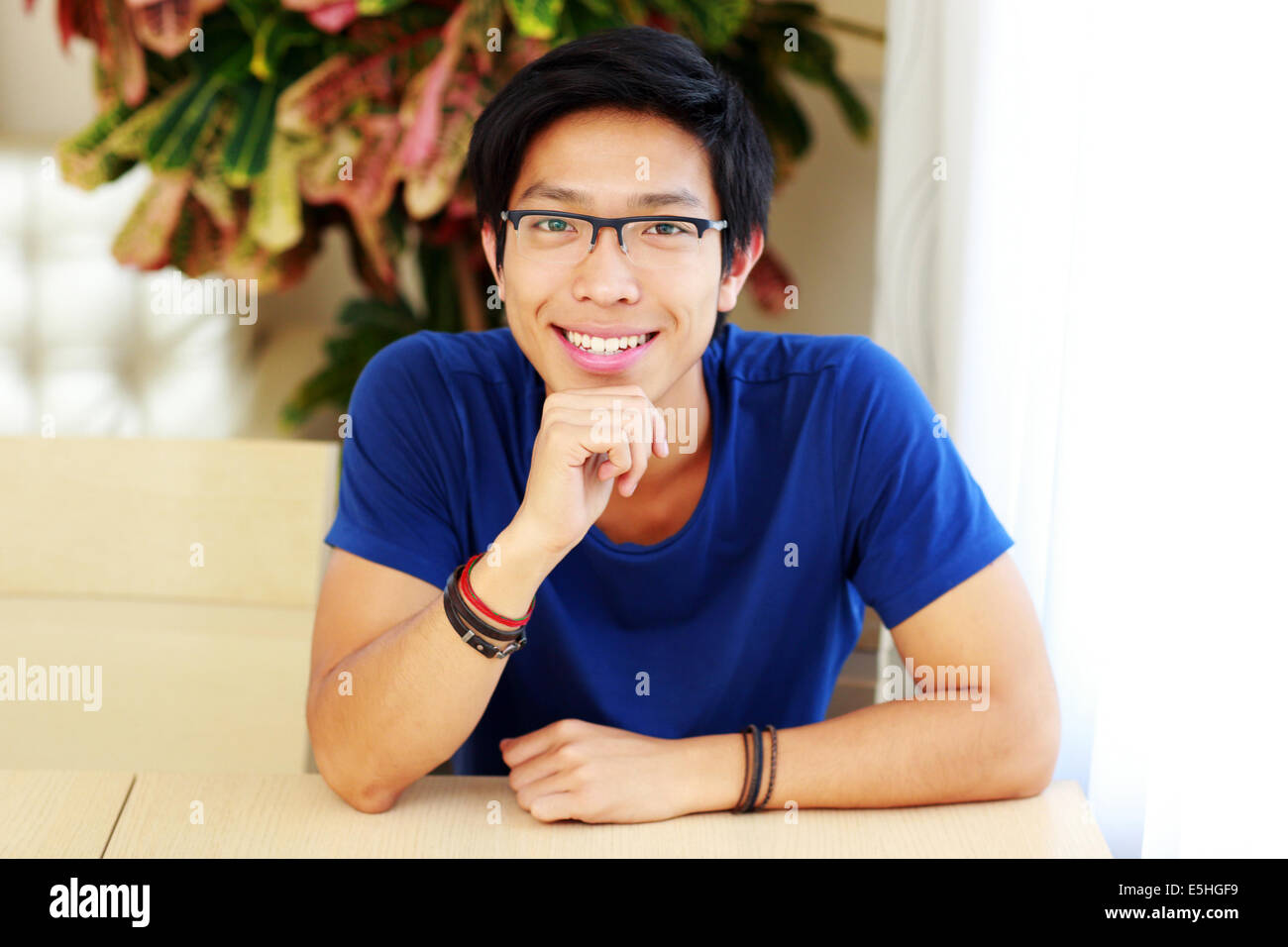 Lächelnde asiatische Mann mit Brille, die am Tisch sitzen Stockfoto