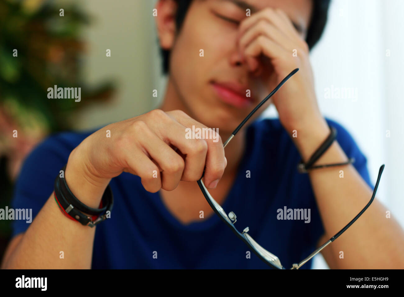 Müde asiatischer Mann mit Augenschmerzen, die Gläser in der hand halten. Gläser im Fokus Stockfoto
