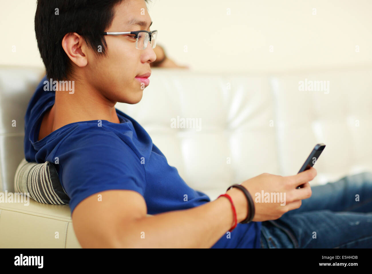 Asiatischer Mann auf dem Sofa liegend und mit Smartphone zu Hause Stockfoto