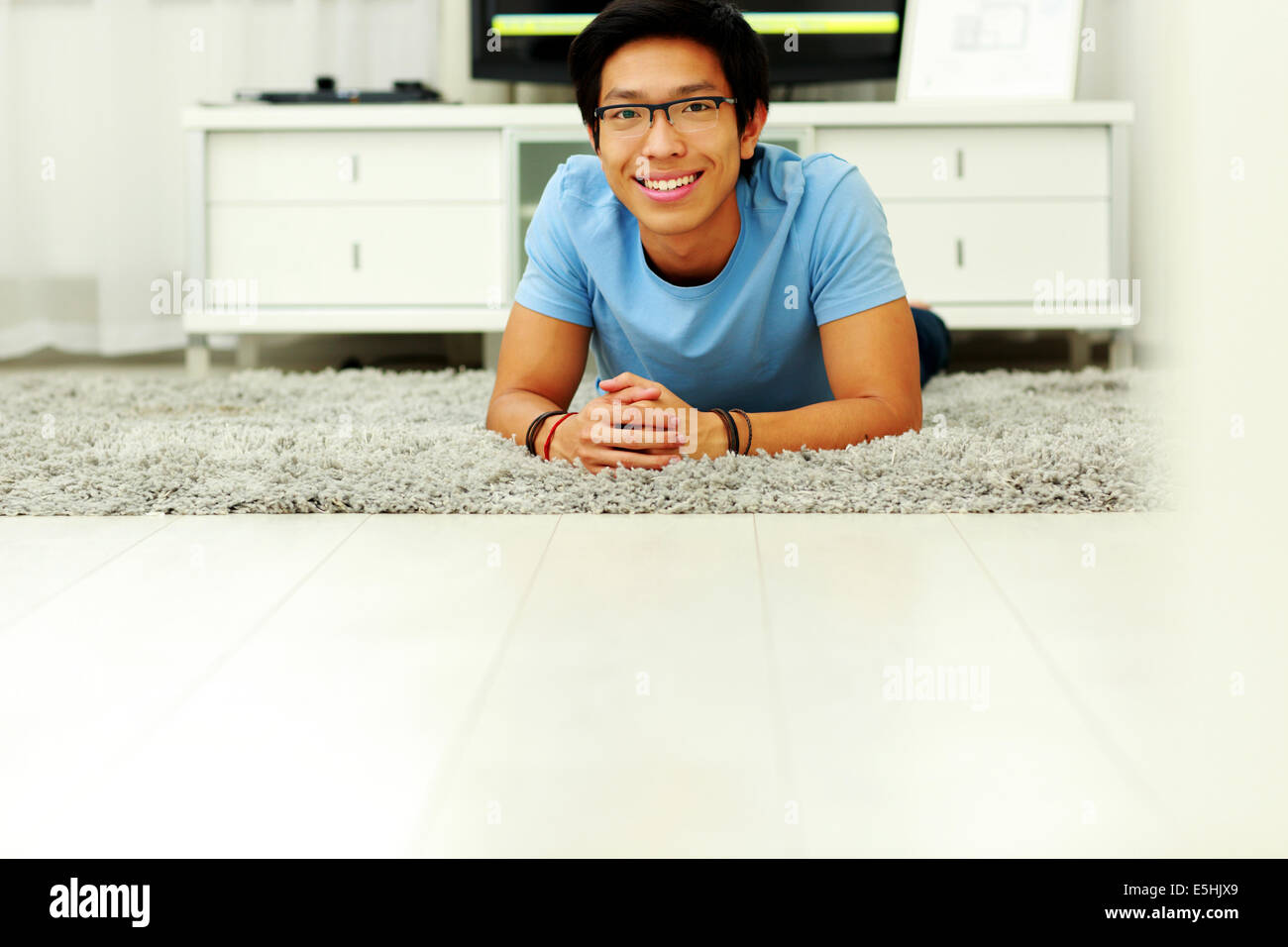 Glücklich asiatischer Mann liegt auf dem Boden zu Hause Stockfoto