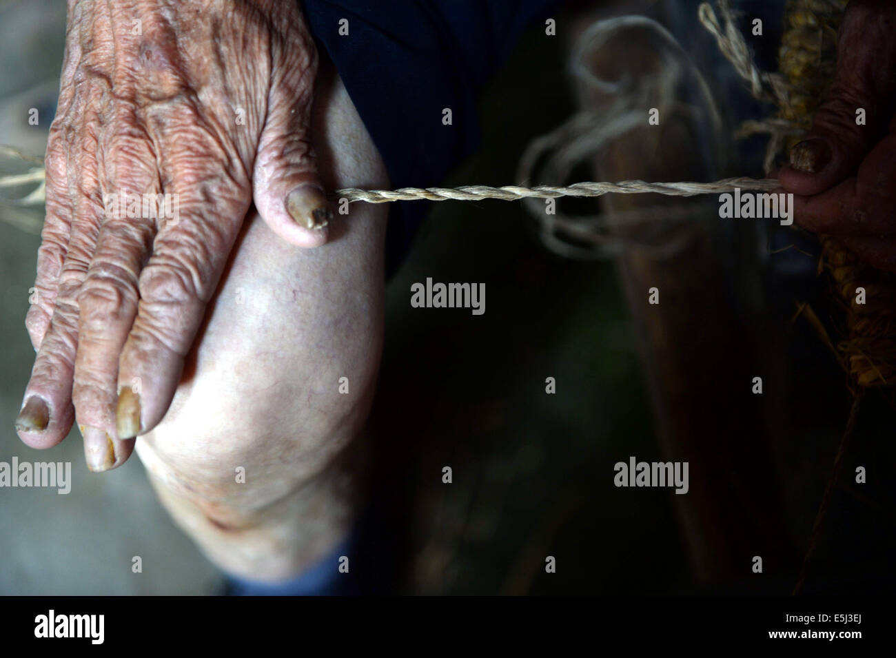 (140802)--YUDU, 2. August 2014 (Xinhua)--Stroh Sandale Handwerker Chen Luoshou macht Kabel durch eine Drehbewegung Ramee zwischen Palm und Oberschenkel, einen Schritt in der Weberei Stroh Sandals, in Buqian Dorf Luoao Township in Yudu County, Osten Chinas Jiangxi Provinz, 1. August 2014. Chen Luoshou, der 78 Jahre alt ist, ist eine der wenige Handwerker in der Lage Stroh Sandalen in Yudu County zu weben. Obwohl niemand Sandalen Stroh heutzutage die siebzigjährige noch in der Weberei Stroh Sandals jeden Tag beibehalten. Ein paar Stroh Sandalen kostet des alten Mannes zwei Stunden und sie sind in der Regel an Touristen oder Messehallen mit 3 verkauft Stockfoto