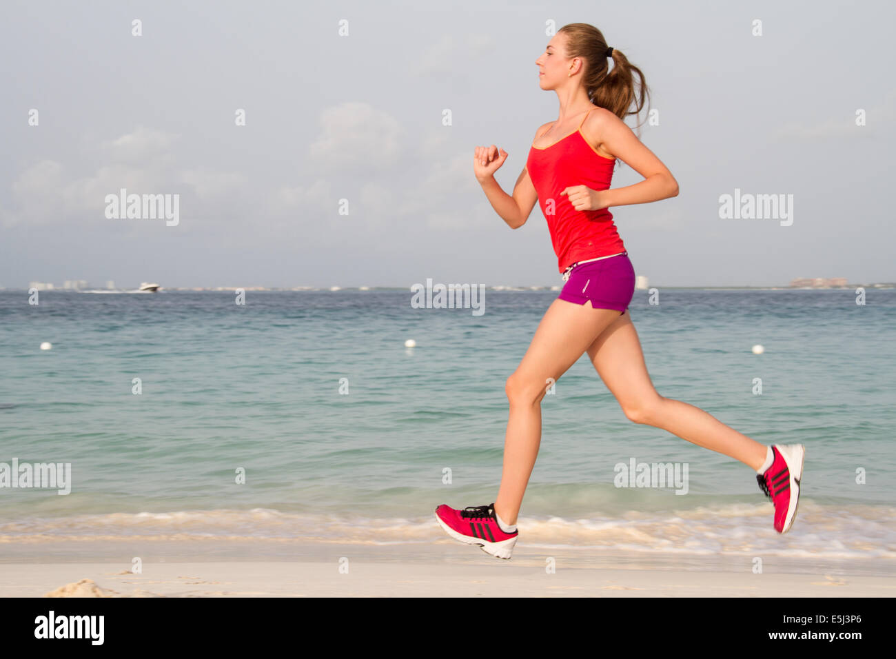 Junge gesunde Frau laufen am Strand in kurzen Hosen Stockfoto
