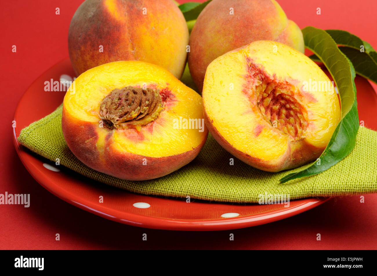 Teller mit leckeren frischen sommerlichen Pfirsiche Obst auf einem roten gepunkteten Teller mit grünen Serviette Serviette vor einem roten Hintergrund. Stockfoto