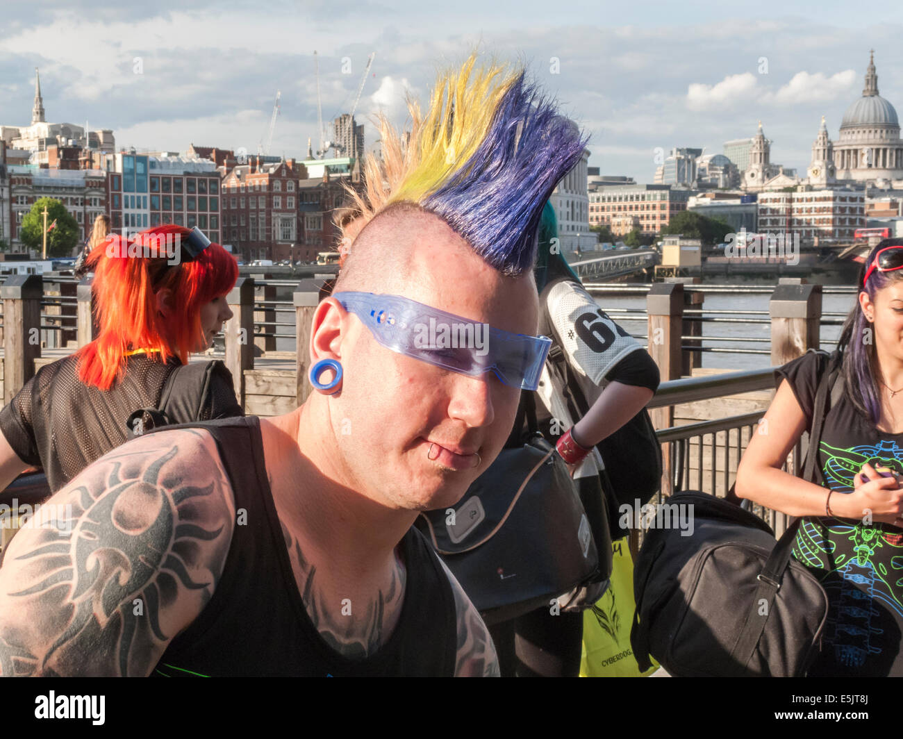 Moderner Lifestyle: Ein junger Mann mit Tattoos, Piercings und ein mehrfarbiges gel Mohican punk Frisur und blauer Sonnenbrille cool, South Bank, London Stockfoto