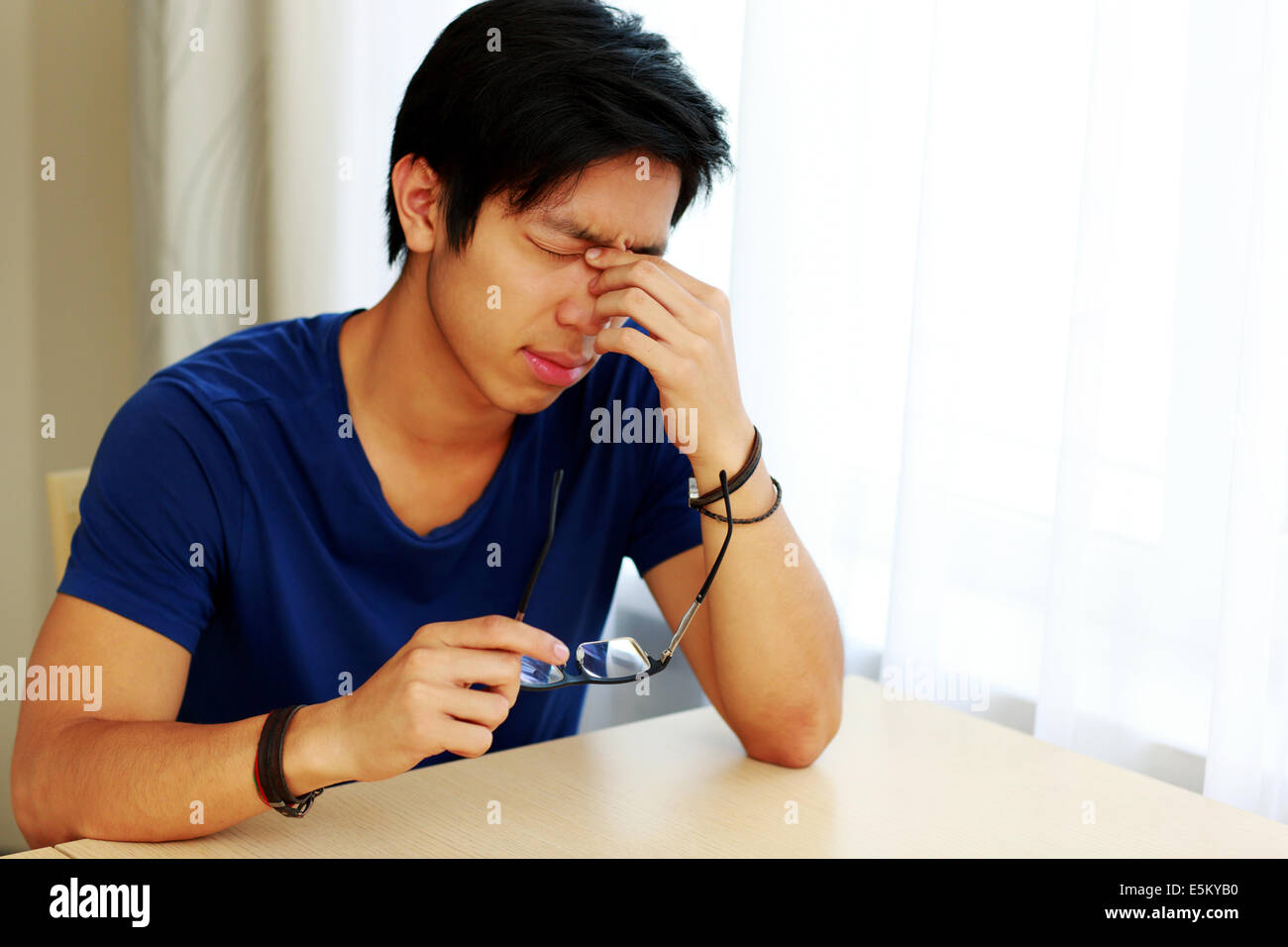 Müde asiatischer Mann mit Augenschmerzen, die Gläser in der hand halten Stockfoto