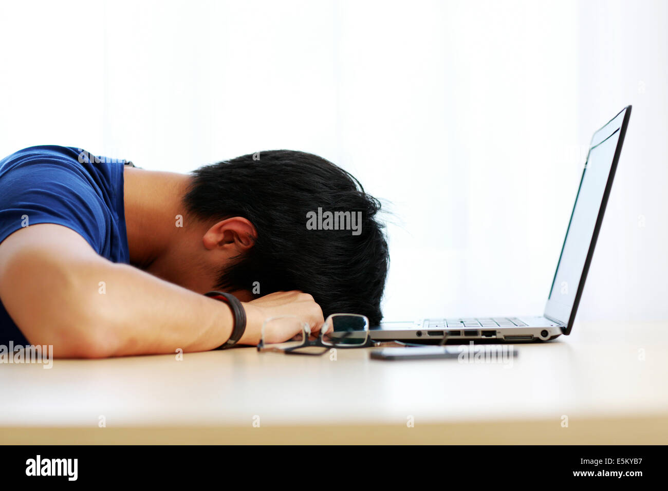 Asiatischer Mann mit Laptop zu Hause auf dem Tisch schlafen Stockfoto