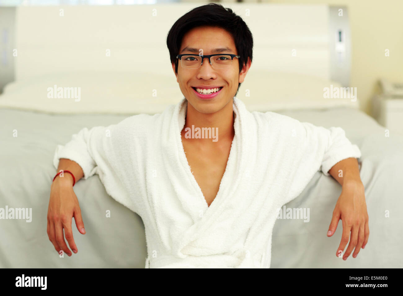 Glücklicher Mann im Bademantel stützte sich auf das Bett im Schlafzimmer Stockfoto
