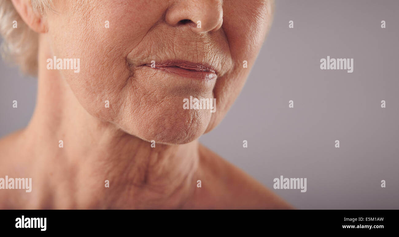 Makro von einem senior Frauengesicht mit faltige Haut vor grauem Hintergrund. Gesicht der alten Frau zugeschnitten. Stockfoto