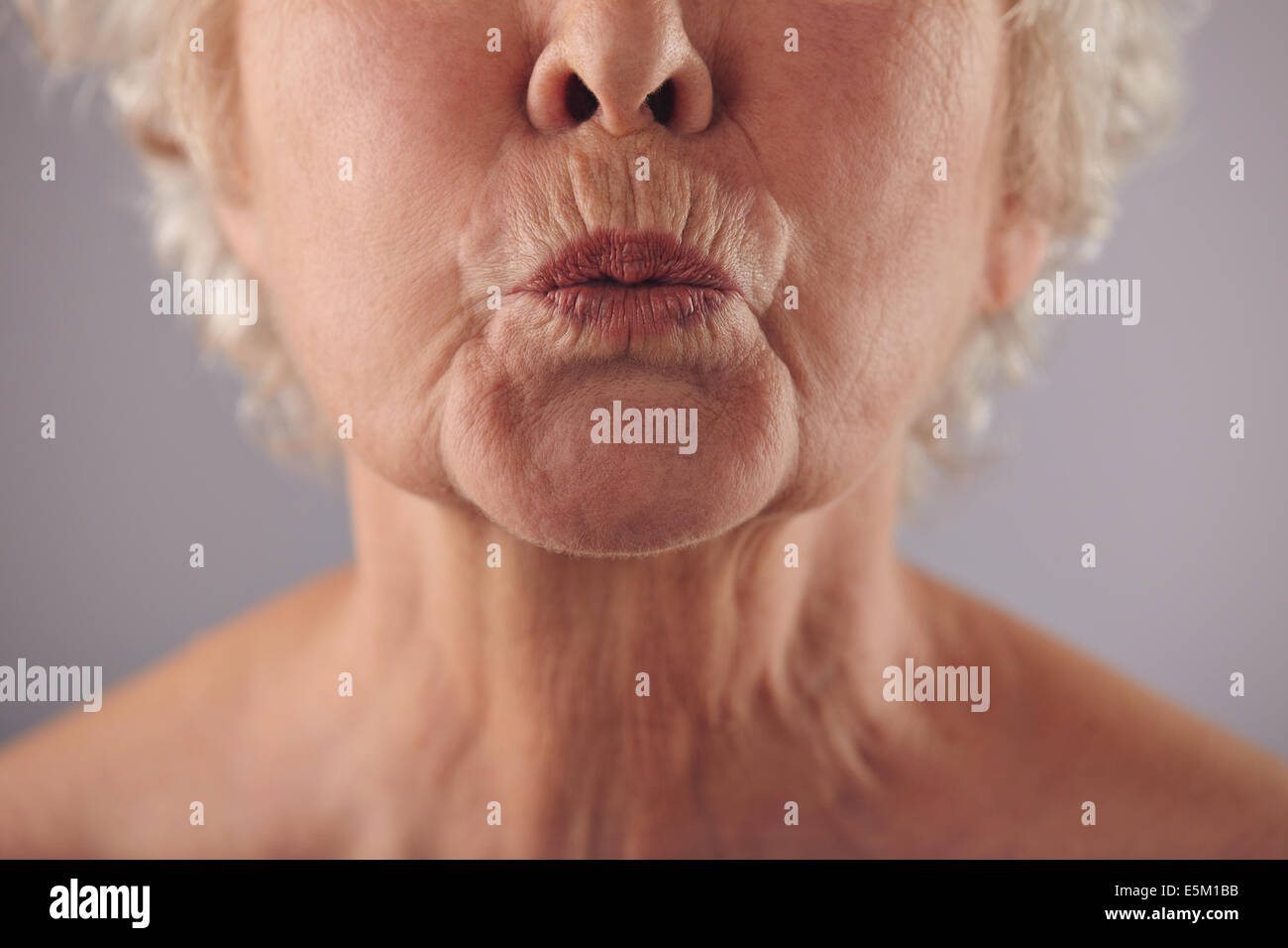 Close-up Portrait Reife Frau Fältelungen Lippen vor grauem Hintergrund. Ältere Frau verzog das Gesicht. Konzentrieren Sie sich auf die Lippen. Stockfoto