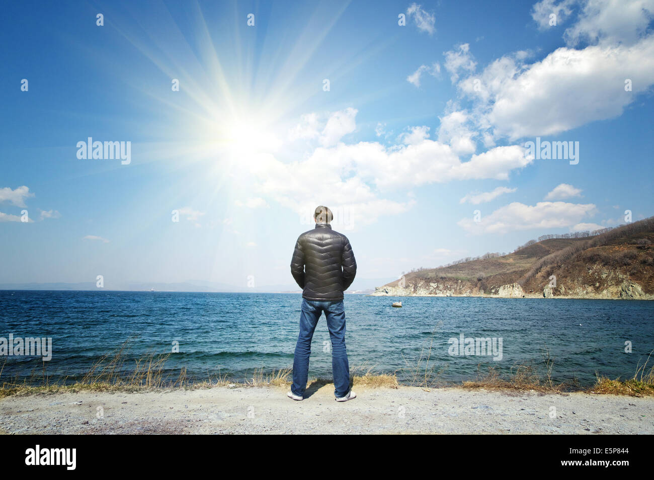 Mann in einem schwarzen Jacke steht am sonnigen Himmel Meer Hintergrund Stockfoto