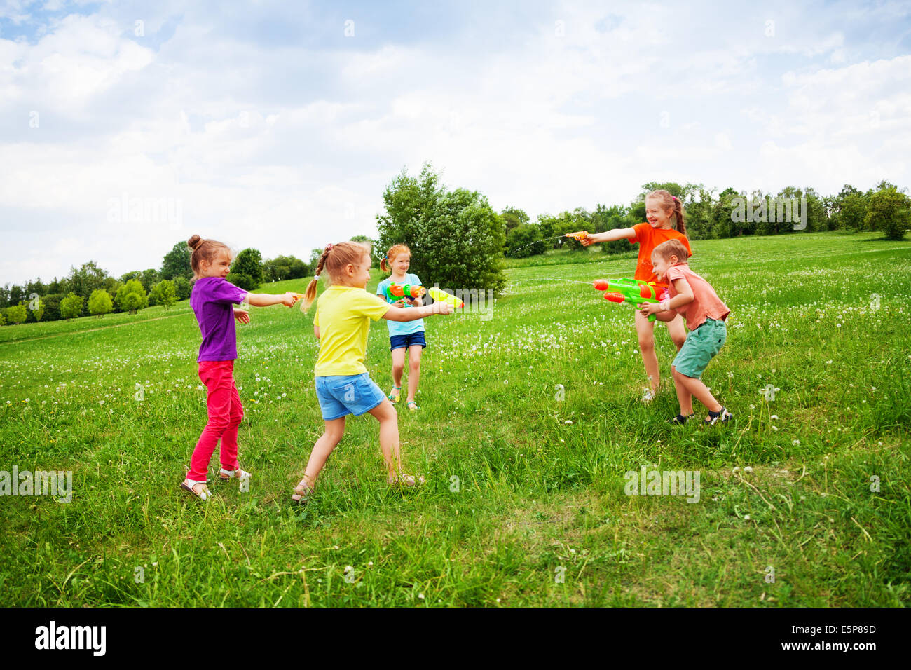 Kinder spielen mit Wasserpistolen auf einer Wiese Stockfoto