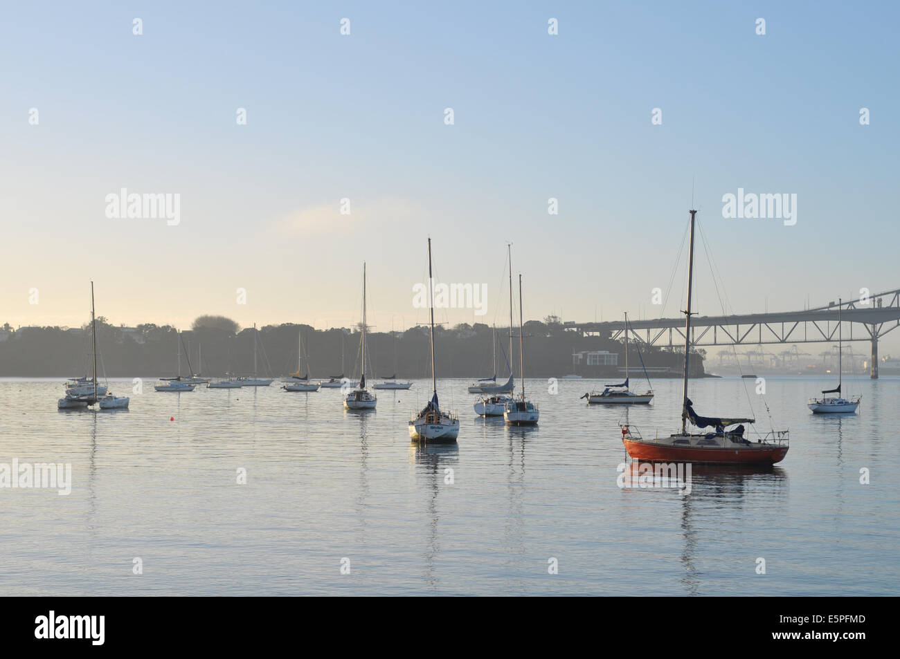 Segelboote verankert auf ruhiger See mit Land und Brücke im Hintergrund Stockfoto