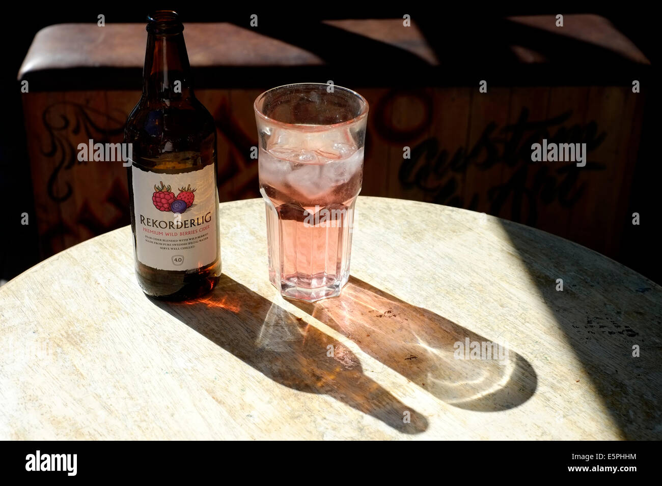 Glas und Flasche Frucht gewürzten Apfelwein saß auf einem sonnenbeschienenen Tisch in einer bar Stockfoto