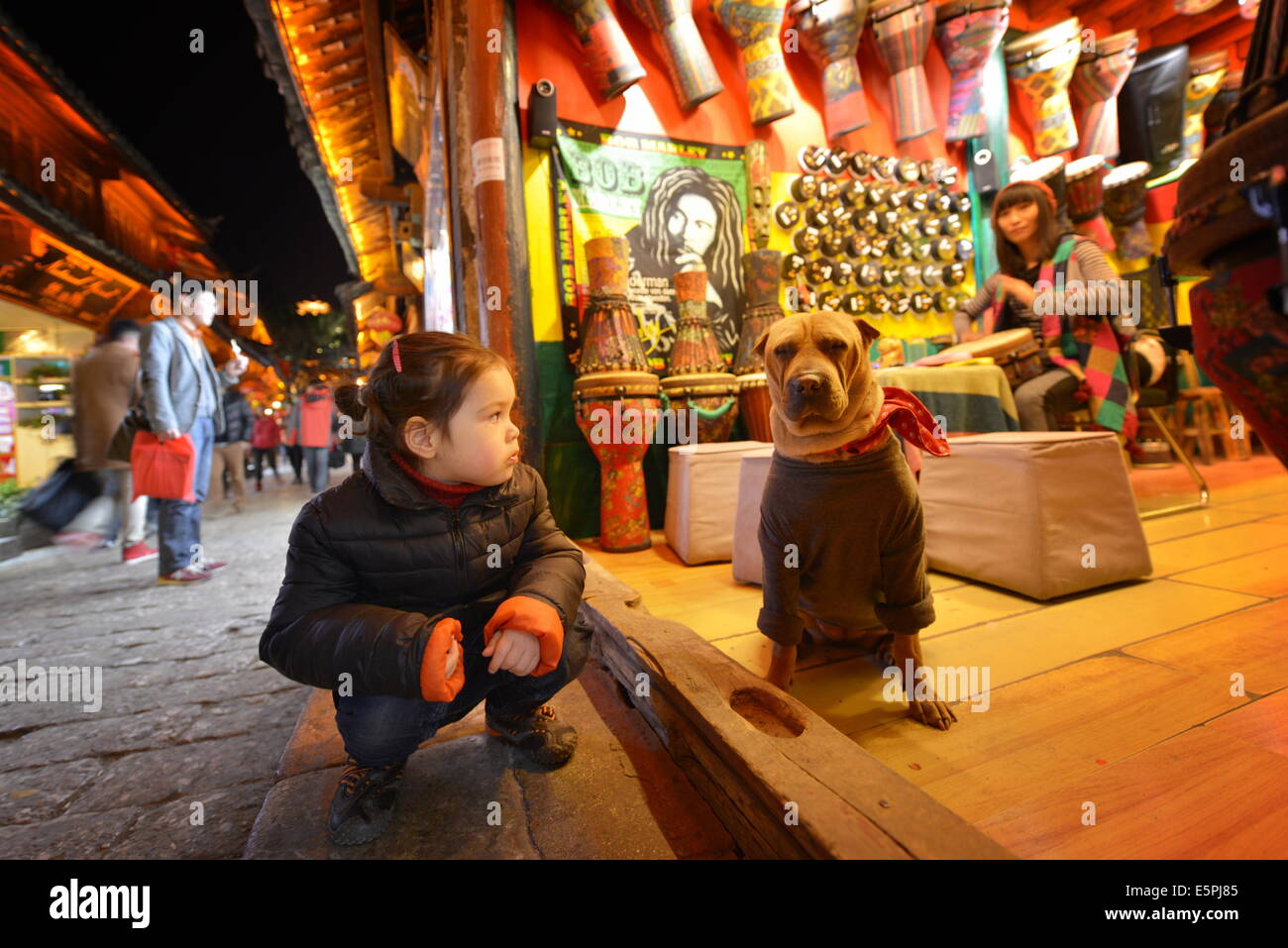 Junges Mädchen sitzt neben einem Hund, der trägt Kopftuch und Pullover, Lijiang, Yunnan, China, Asien Stockfoto