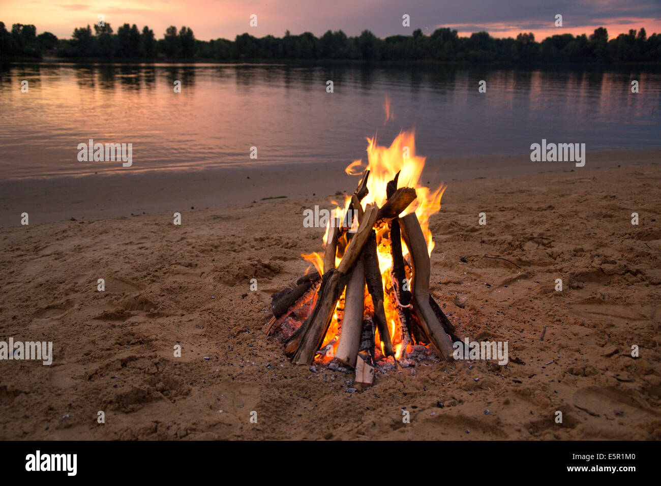 Lagerfeuer am Ufer des Flusses bei Sonnenuntergang Stockfoto