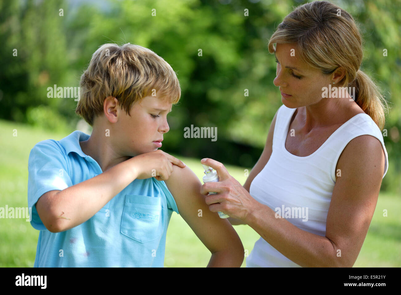 Frau Anwendung Spray auf juckende Haut ihres Sohnes nach Insektenstich. Stockfoto