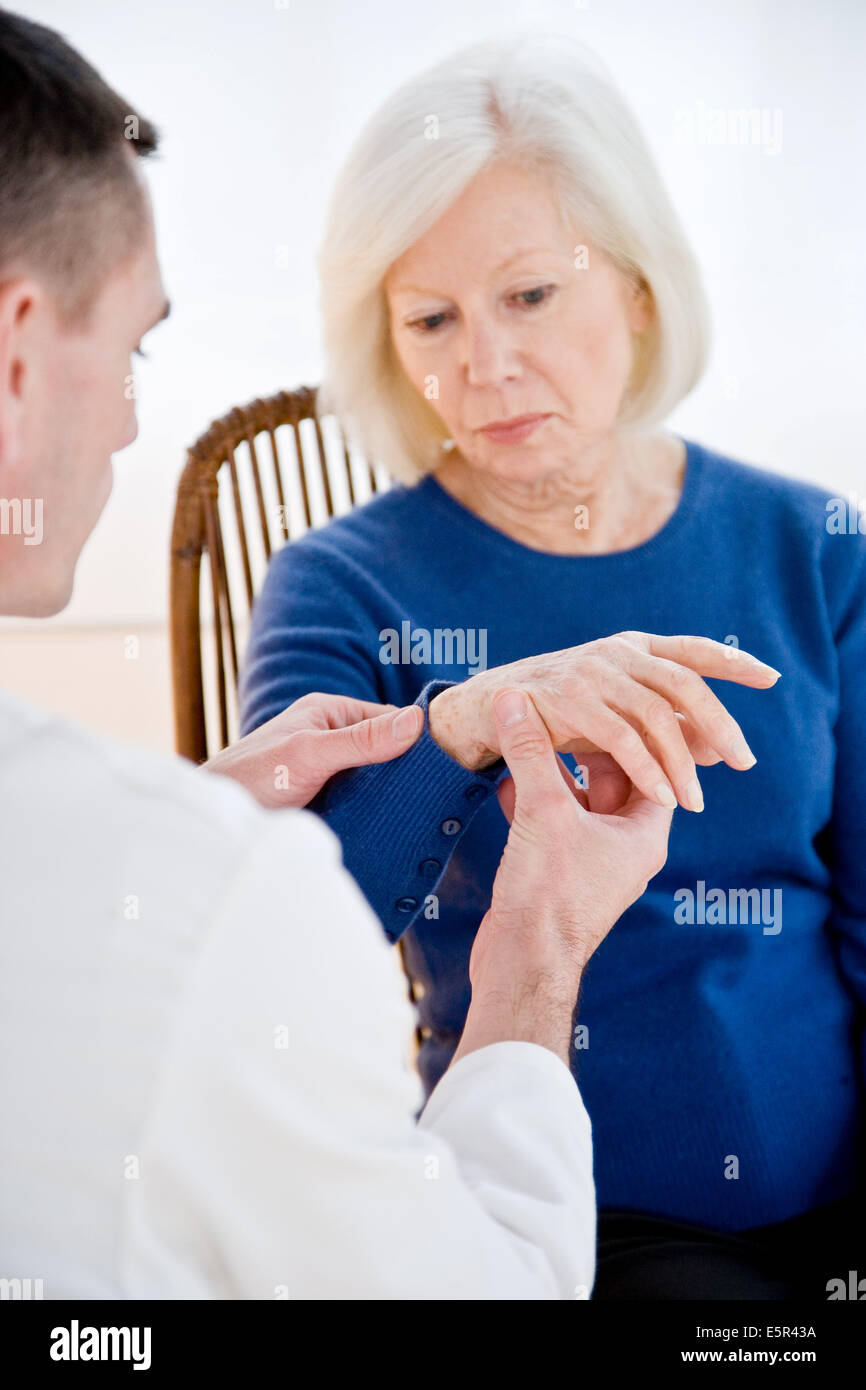 Arzt untersucht das Handgelenk der Seniorin. Stockfoto