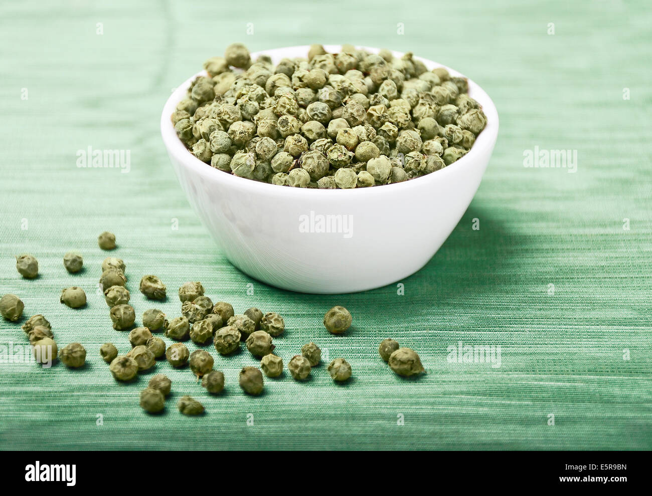 Paprika - gemacht getrocknete grüne Pfefferkörner in eine weiße Porzellanschale auf grüne Textilien aus Leinen. Stockfoto