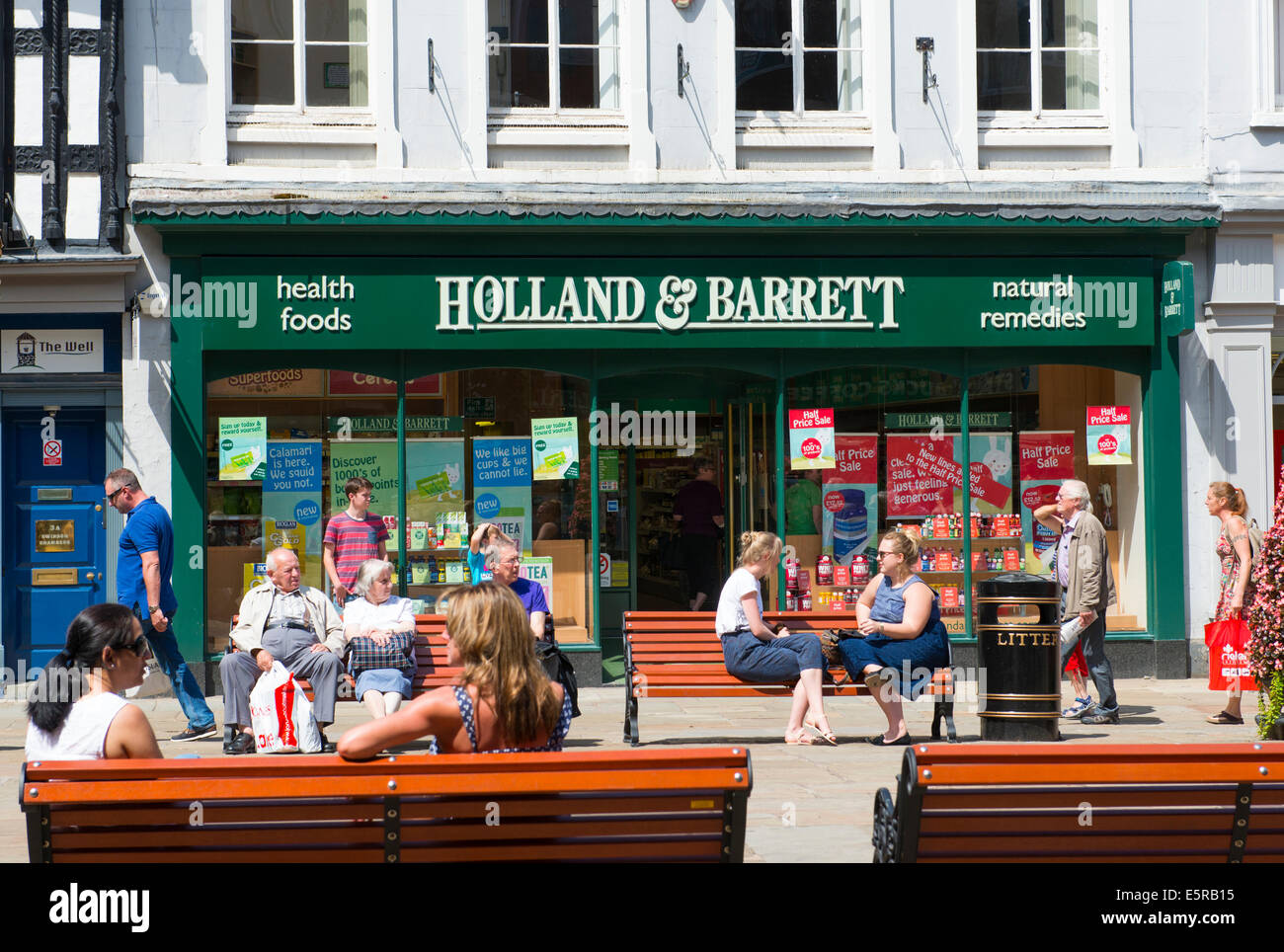 Menschen sitzen vor einem Holland & Barrett-Geschäft in Shrewsbury, Shropshire, England, UK Stockfoto