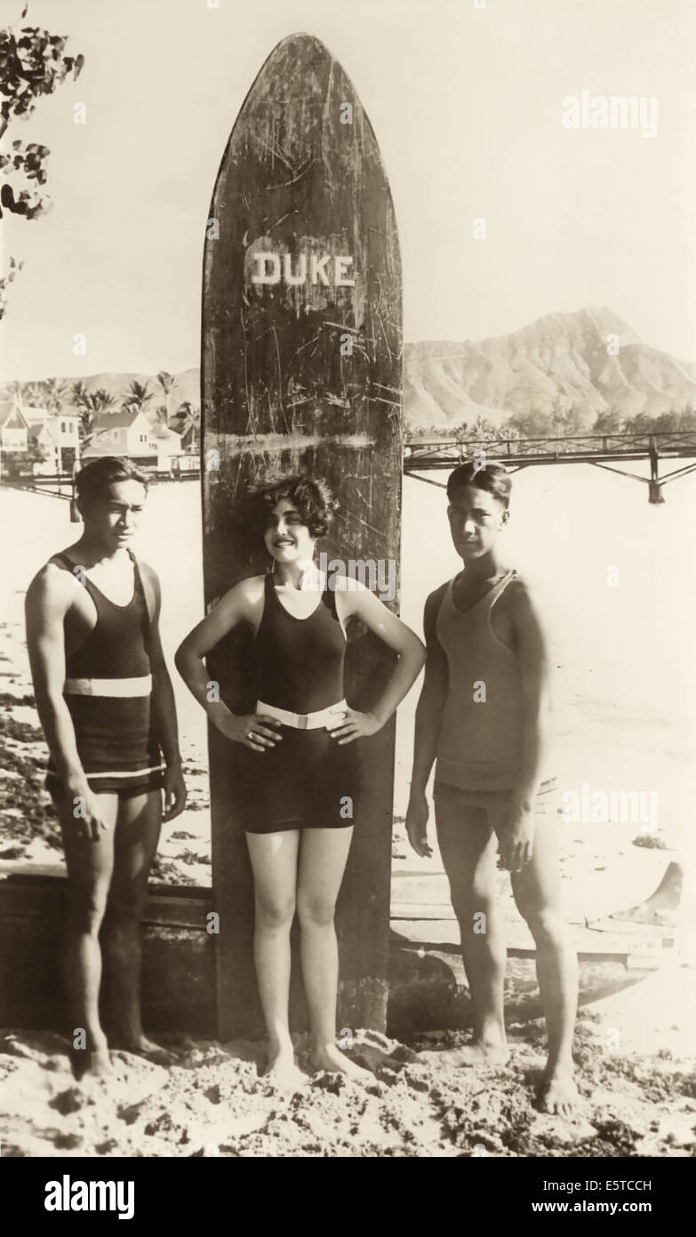 Verpassen Sie Honolulu 1925, Caroline "Leilani" Deas mit legendären Surfer Duke Kahanamoku Surfbrett, die sie Ritt am Strand. Stockfoto