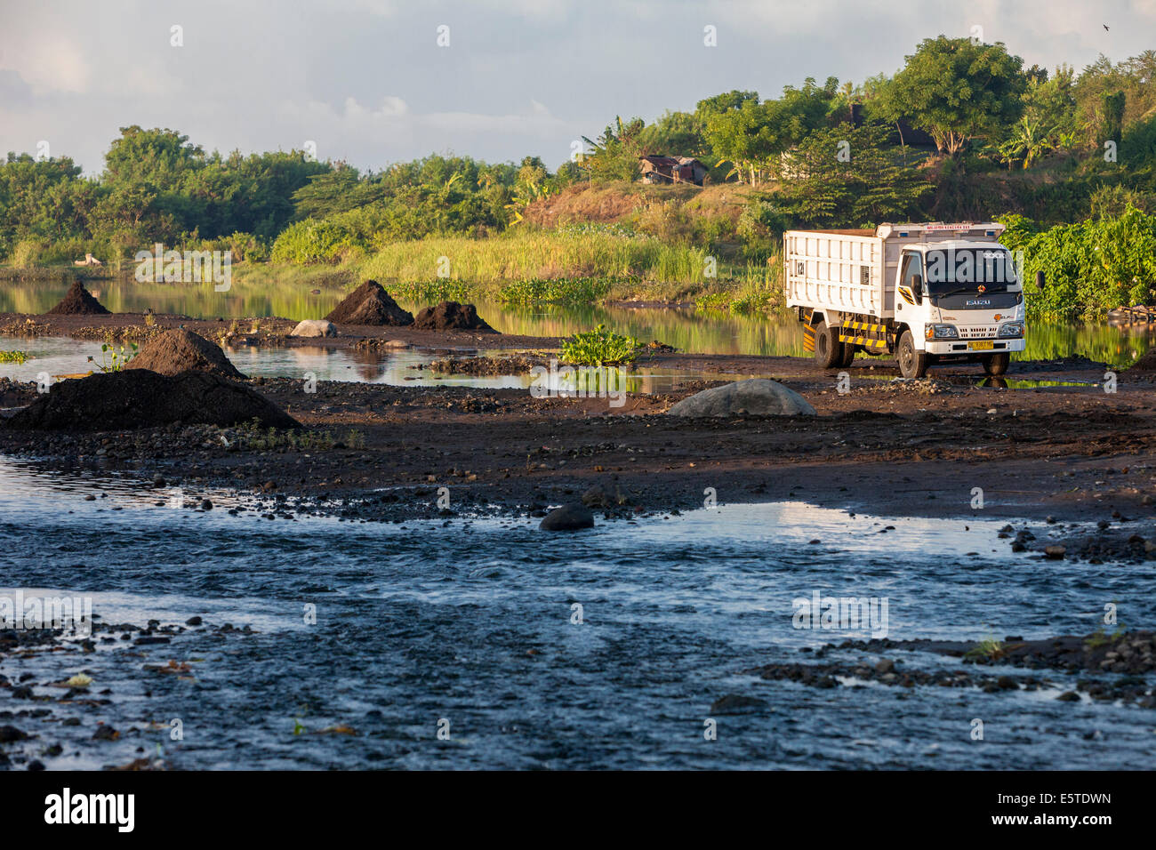 Bali, Indonesien.  LKW Abholung schwarzen Vulkanerde vom Flussbett zu ergreifen, um Felder zur Anreicherung des Bodens. Stockfoto
