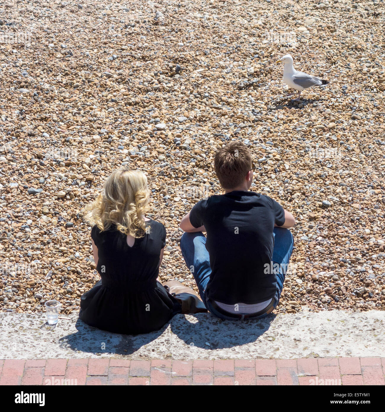Junges Paar sitzt im Chat am Kiesstrand Stockfoto